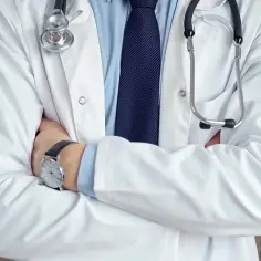 Lekarz w białym kitlu ze stetoskopem i zegarkiem na ręce, ze skrzyżowanymi ramionami.
