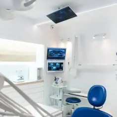 Nowoczesny gabinet stomatologiczny z fotelem, monitorami RTG i sprzętem dentystycznym.