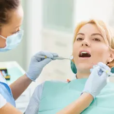 Dentystka w masce bada zęby pacjentki przy użyciu lusterka i sondy.