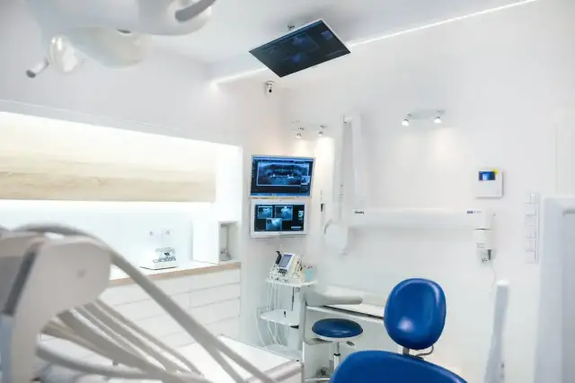 Nowoczesny gabinet stomatologiczny z fotelem, monitorami RTG i sprzętem dentystycznym.